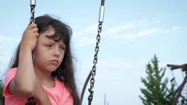 Friendless child on playground. A little gir with sad face expresion sits on swing on playground.