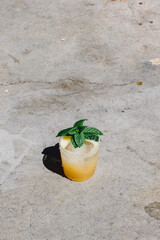 Obraz premium yellow cocktail drink in double old fashioned glass with ice and fresh mint garnish in direct sunlight on concrete