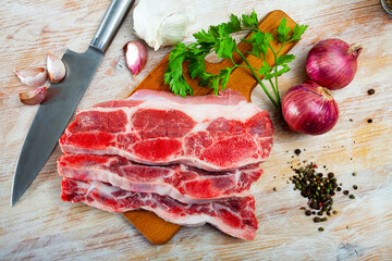 Raw beef with streaks of fat on kitchen table with red onion, garlic and parsley
