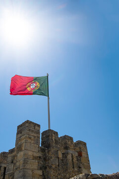 the national flag of portugal flies on top of a battlement of the castle of St. George in Lisbon on a sunny day, blue sky