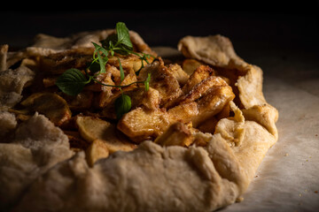 Rustic apple galette on parchment paper garnished with a sprig of mint.