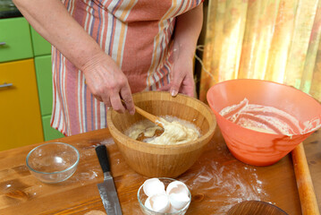 Obraz na płótnie Canvas Female hands mixing dough in bowl with wooden spatula in home kitchen. Close-up selective focus.