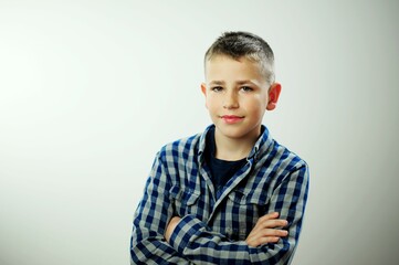 Satisfied smiling caucasian kid boy wearing plaid shirt over white background, smiling schoolboy in a plaid shirt stands with his arms crossed on his chest