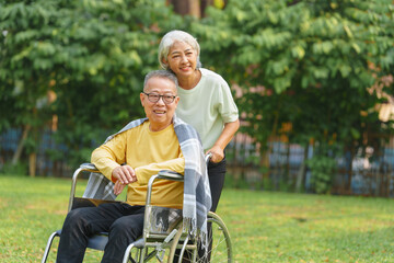Fototapeta na wymiar Elderly couple husband and wife happy asian people giving love and care Wheelchair in the park relaxing in spring, relaxing and walking outside at the park.