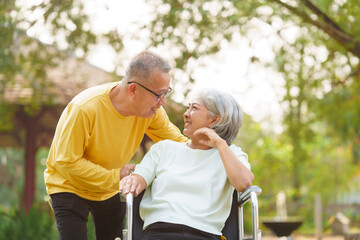 Elderly couple husband and wife happy asian people giving love and care Wheelchair in the park relaxing in spring, relaxing and walking outside at the park.