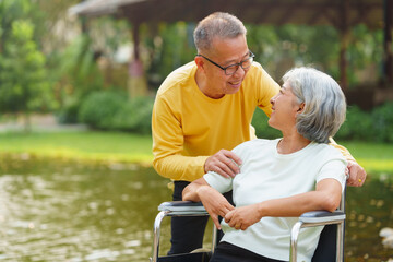 Elderly couple husband and wife happy asian people giving love and care Wheelchair in the park relaxing in spring, relaxing and walking outside at the park.