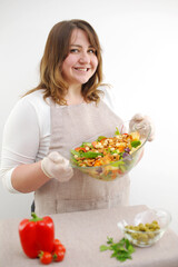Obraz na płótnie Canvas Smiling young woman serving fresh salad on plate. Happy smiling cute woman cooking fresh healthy vegan salad at home with many vegetables in kitchen and trying new recipe High quality photo