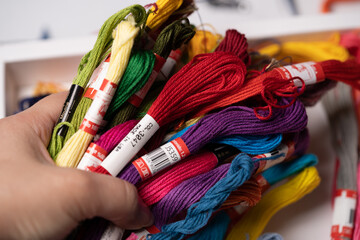 Mano sosteniendo montón de madejas de hilo para bordar de colores variados