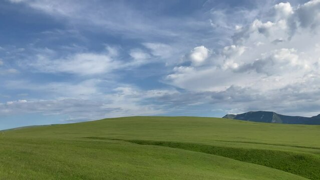Overarching panorama from Piani di Ragnolo with path, bucolic Windows XP style green hills, camera panning right and reaching Strada Provinciale 5 below and the Sibillini Mountains under a cloudy sky