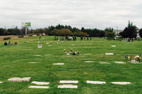 parque cementerio con pasto verde flores personas en las tumbas mostrando respeto en un d&iacute;a nublado.