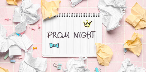 Notebook with text PROM NIGHT and crumpled paper sheets on pink tile background