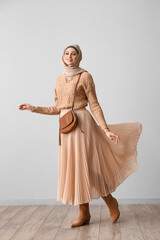 Stylish Muslim woman in beige hijab with bag near light wall