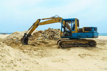 Excavator with a bucket stands on the sand on the beach