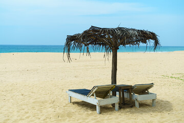 Wooden sun loungers and straw umbrella on the beach