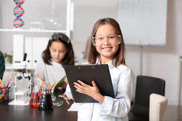 Little girl with safety goggles and clipboard in science classroom