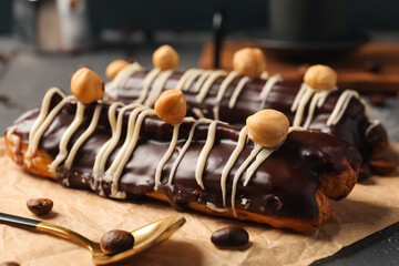 Parchment with delicious chocolate eclairs, hazelnuts and coffee beans on black wooden table