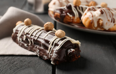 Delicious chocolate eclair with hazelnuts on black wooden table, closeup