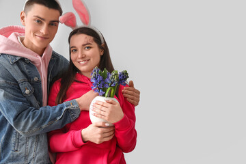 Happy young couple in bunny ears with flowers on grey background. Easter celebration