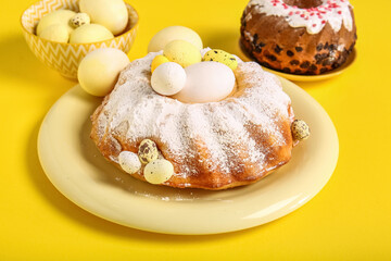 Plate with sweet Easter cake and painted eggs on yellow background
