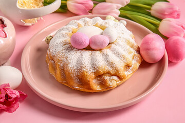 Plate with tasty Easter cake and painted eggs on pink background, closeup