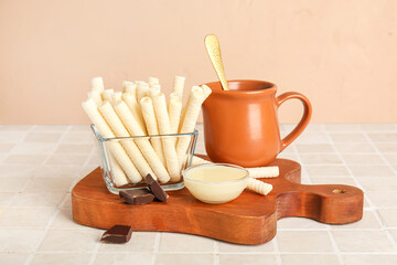 Board with delicious wafer rolls, condensed milk and chocolate pieces on tile table