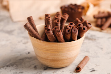 Bowl with delicious chocolate wafer rolls on beige background