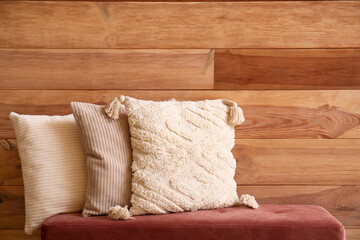 Stylish decorative pillows on bench near wooden wall