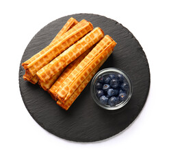 Slate board with delicious wafer rolls and blueberries isolated on white background