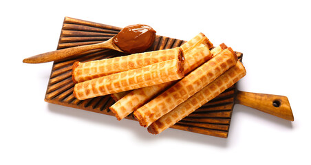 Board with delicious wafer rolls and spoon of boiled condensed milk isolated on white background