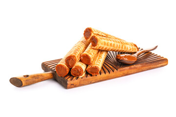Board with delicious wafer rolls and spoon of boiled condensed milk isolated on white background