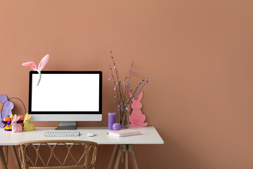 Workplace with computer, tree branches and Easter eggs in vase near color wall