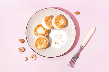 Plate with tasty cottage cheese pancakes and sour cream on pink background