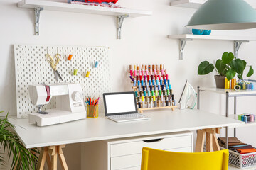 Tailor's workplace with laptop, sewing machine and thread spools in atelier
