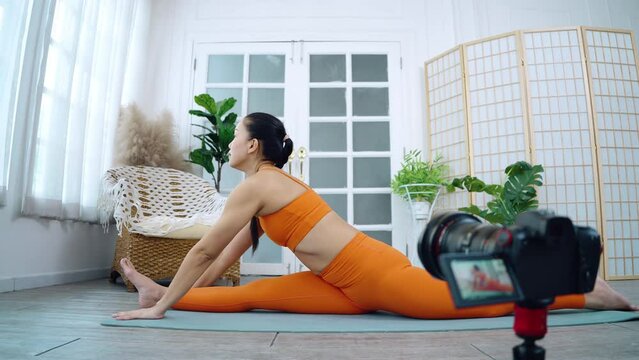 Asian women doing yoga while shooting a social media video, Blogging for at-home online learning.  38-year-old woman stretching in Janu Sirsasana or Head to Knee Pose, Seated forward bend pose