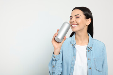 Beautiful happy woman drinking from beverage can on light grey background. Space for text