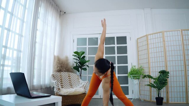 Asian women live streaming yoga online with a laptop, Blogging for at-home online learning. 38-year-old woman stretching in Triangle Pose.