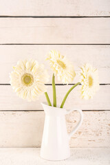 Vase with beautiful gerbera flowers on table near wooden wall