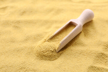 Wooden spoon of granulated brewer`s yeast on powder, closeup