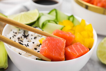Delicious poke bowl with salmon, lime and vegetables on table, closeup