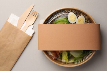 Tasty food in container with wooden fork and knife on light background, flat lay. Space for text