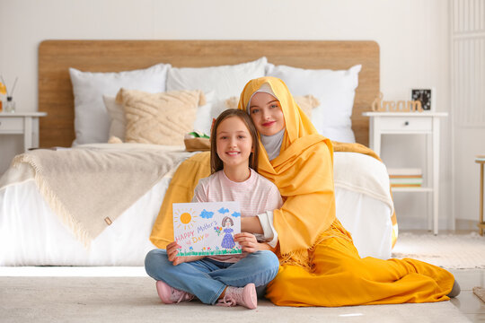 Little girl with drawing for Mother's Day and her Muslim mom in bedroom
