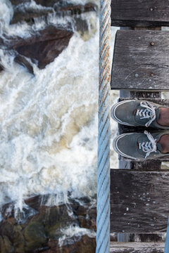 Blick von oben auf Füße auf Brücke in das Wasser eines Flusses