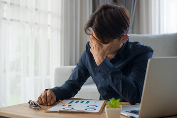 The young businessman sat at his desk, he held his head in his hands due to fatigue and headache from long hours of work bad vision sight problem sit at home table using laptop.