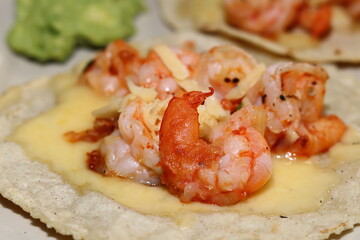 A taco of shrimp on a tortilla with melted cheese and a guacamole 