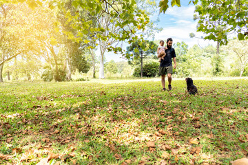 Father holding his baby walking with his dog.