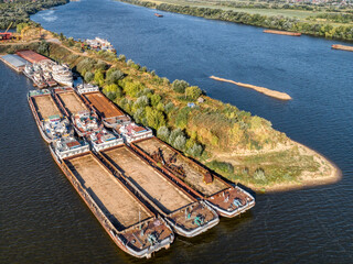Dry cargo barges stand empty moored to green river island