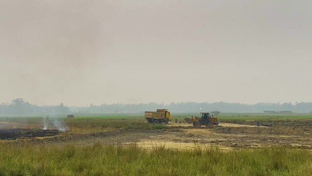 Bulldozer excavating earth removal next to smoking ash construction site, Bangladesh