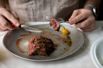 Close-up of plate with perfect rare cooked steak and male hands on table.Man eating meat.People and...
