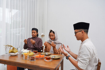 Asian Muslim family praying before having Iftar dinner. Eating traditional Indonesian food during Ramadan feasting month at home. 
