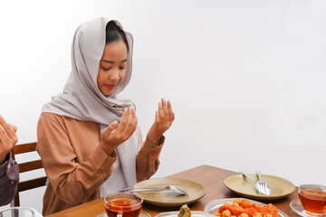 Asian Muslim woman praying before having Iftar dinner. Eating traditional Indonesian food during...
